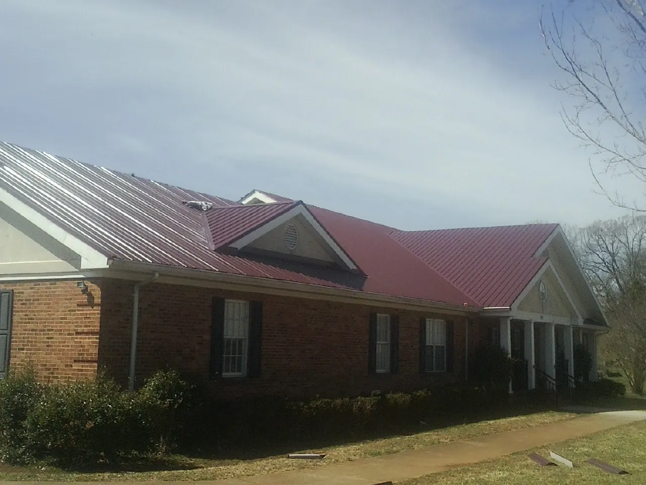 Red metal roof with gabled entries on a long brick building, from a Hail Damage Roof Repair job in Richboro