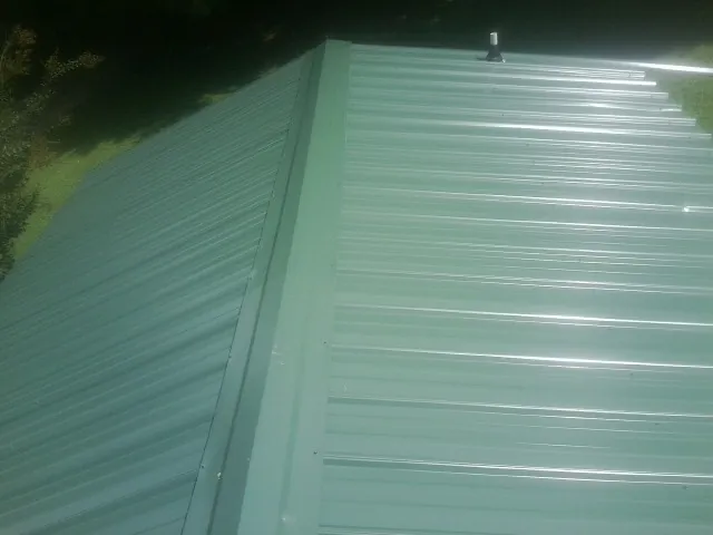 New green metal panels meeting at the ridge of a roof — Flat Roof Repair work by our crew in Richboro