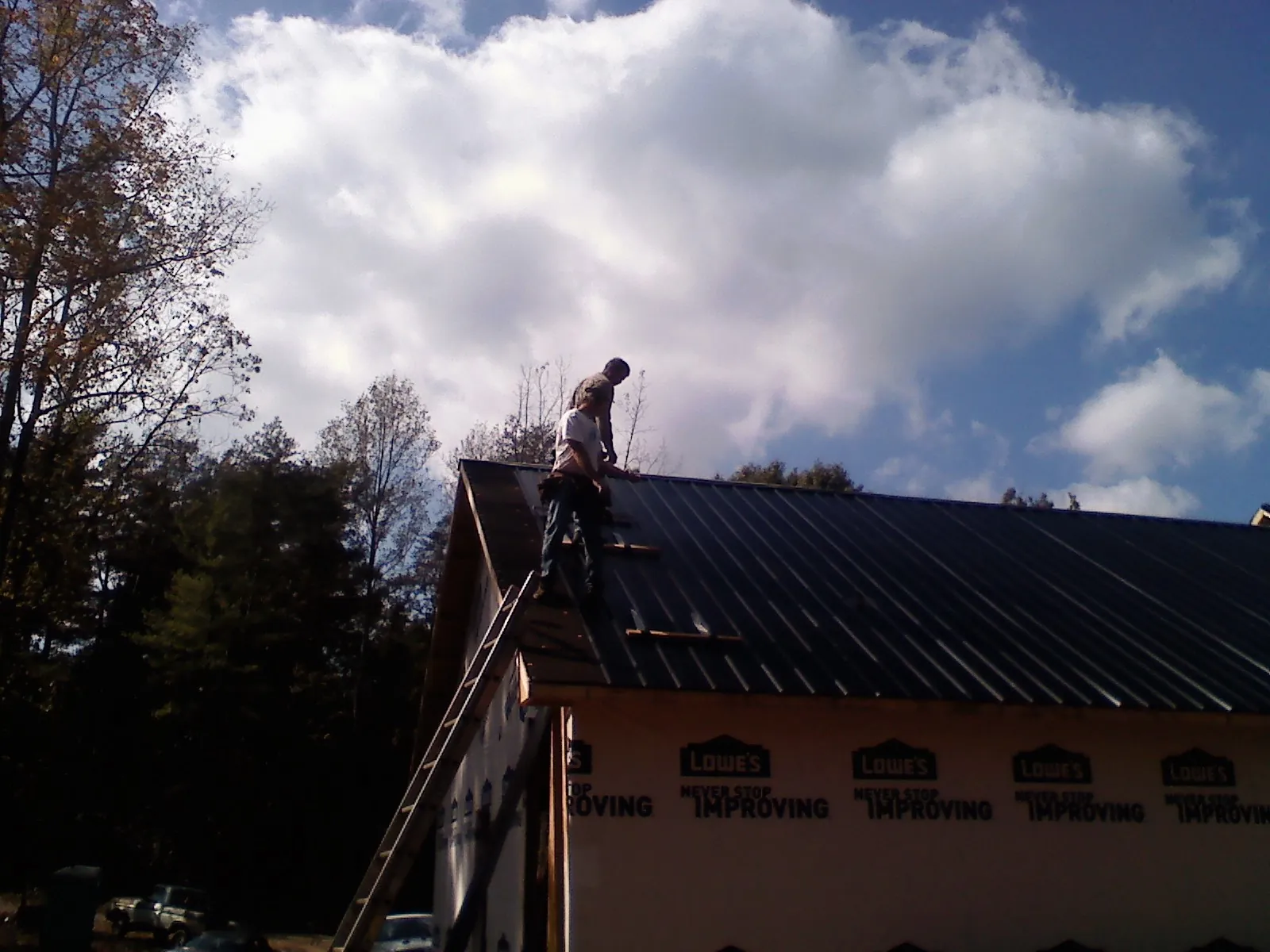 Roofer fastening dark metal panels high against a cloudy sky, from a Roof Inspection job in Richboro