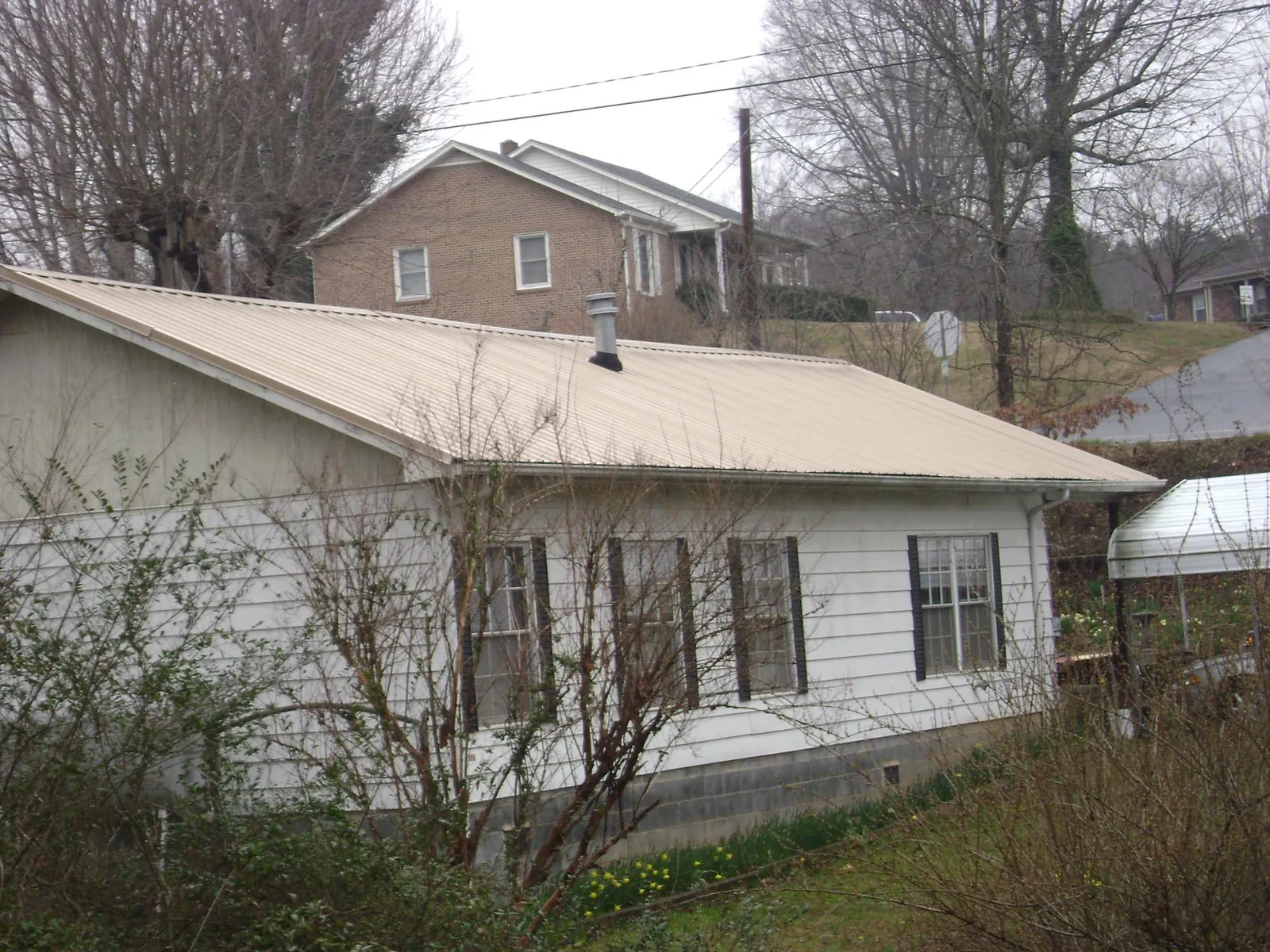 Tan metal roof on a white sided house set into a hillside in Richboro